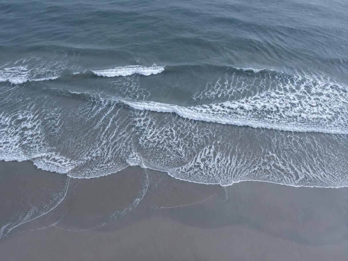 Aerial view of tide lines and foam receding over wet sand